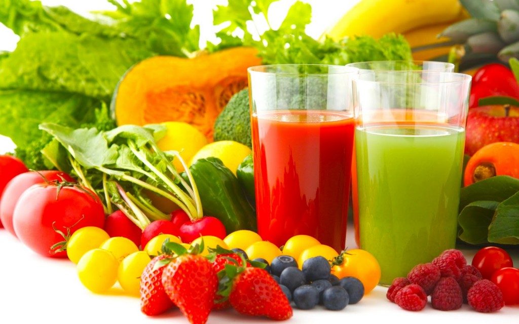 Diversas frutas y verduras con dos vasos de jugo verde y rojo